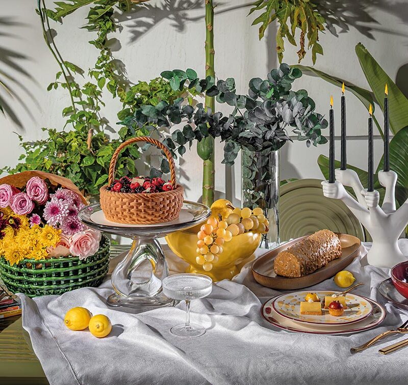 Groove Obroun table de Tom Dixon, centre de table Damo et panier en céramique de Ferm Living chez Clay Concept Store Nappe de table Le Jacquard Français chez Descamps Set de table Steel de Couzon, bougeoir Eve Hands de Jonathan Adler chez Rouge Ivoire Boite florale décorative chez Chabi Chic Assiette profonde La Mère de Serax chez Hagen Service de table Aura de Sarah Lavoine et assiette à dessert Terra Wine de L'Objet chez Nuances Maisons Bûche chez Les Ateliers du Chef Gâteau Le Panier de Chef Hajar Hour