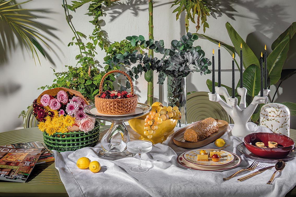 Groove Obroun table de Tom Dixon, centre de table Damo et panier en céramique de Ferm Living chez Clay Concept Store Nappe de table Le Jacquard Français chez Descamps Set de table Steel de Couzon, bougeoir Eve Hands de Jonathan Adler chez Rouge Ivoire Boite florale décorative chez Chabi Chic Assiette profonde La Mère de Serax chez Hagen Service de table Aura de Sarah Lavoine et assiette à dessert Terra Wine de L'Objet chez Nuances Maisons Bûche chez Les Ateliers du Chef Gâteau Le Panier de Chef Hajar Hour